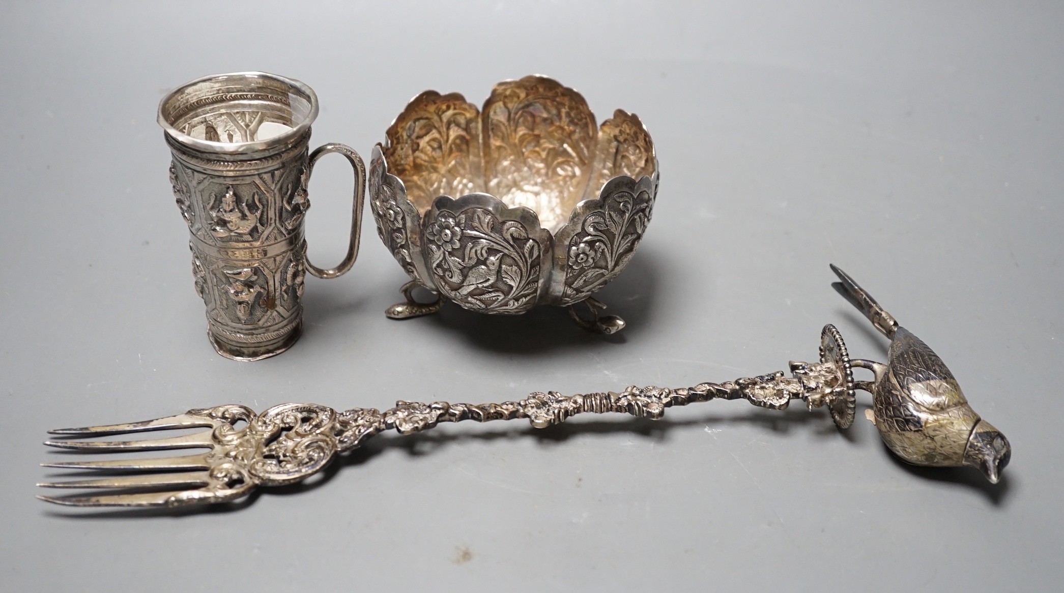 A Dutch white metal toasting fork, with pepperette? finial modelled as a bird, 28.5cm, an Indian white metal double measure cup and a similar bowl.
